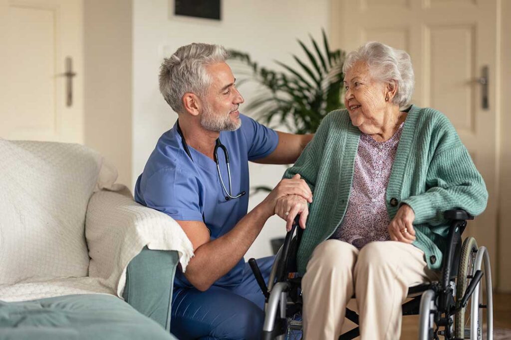 An elderly woman sits at a table reviewing documents with a caregiver, both smiling and talking.
