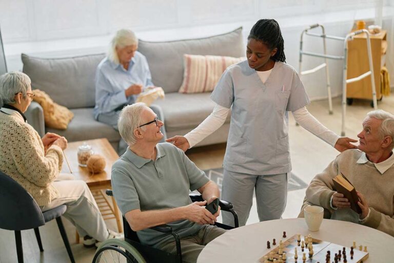 Two seniors chatting over coffee in a sunny, comfortable common area of an assisted living community.